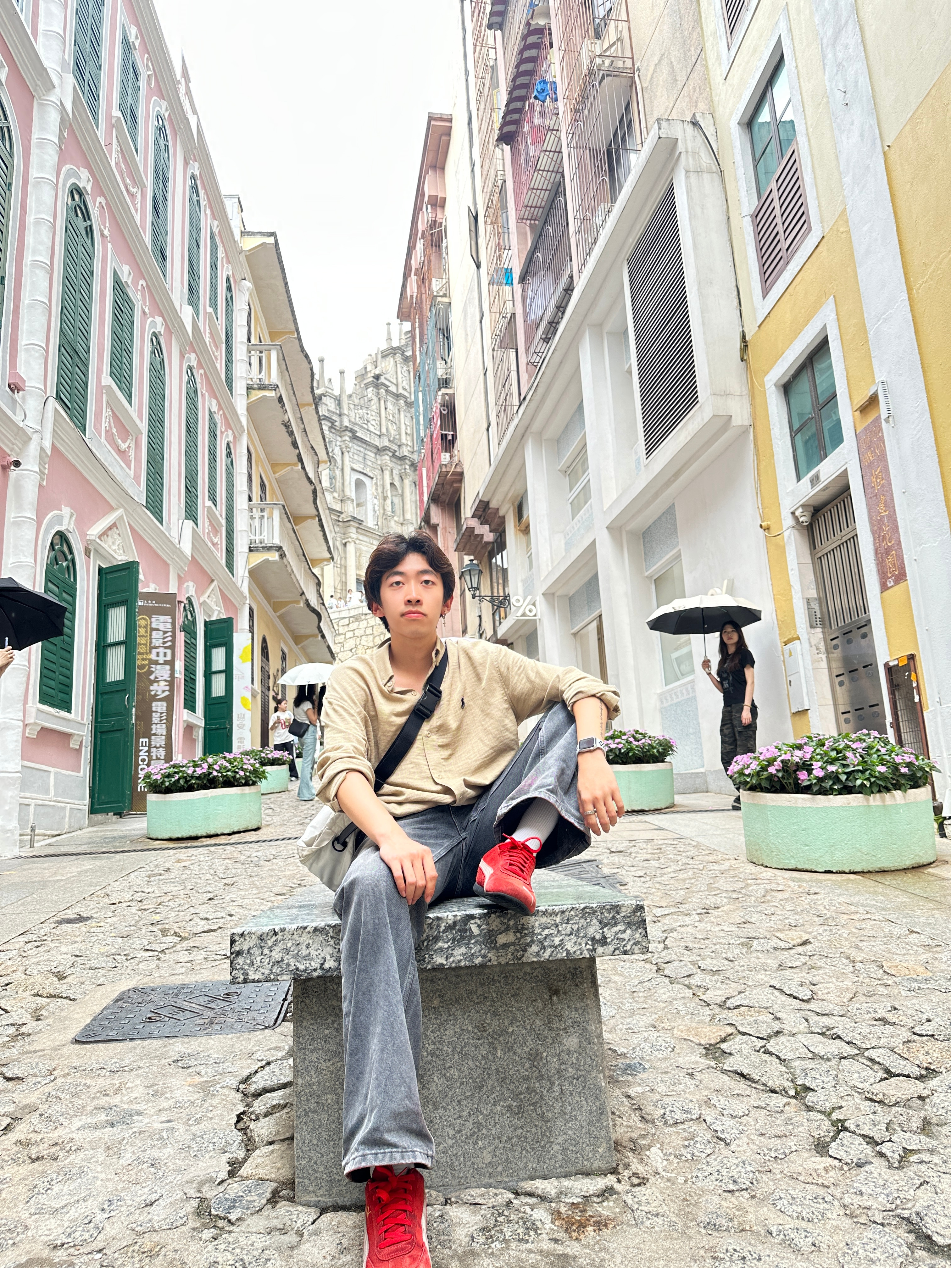 Linfeng Fan seated on a stone bench in a colorful streetscape.